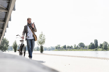 Älterer Mann mit Fahrrad und Smartphone am Rheinufer - UUF14000