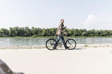 Älterer Mann mit Fahrrad und Smartphone am Rheinufer - UUF14004