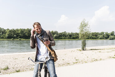 Älterer Mann mit Fahrrad, Smartphone und Kopfhörer am Rheinufer - UUF14005