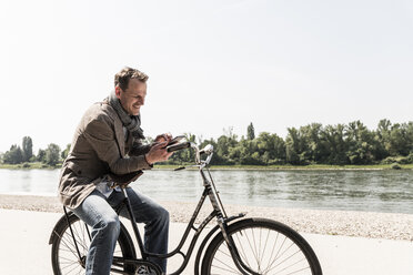 Älterer Mann mit Fahrrad und Smartphone am Rheinufer - UUF14009