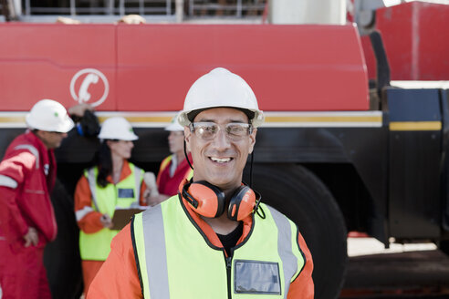 Happy engineer on oil rig, colleagues working in background - ISF07491