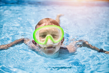 Porträt eines Jungen mit grüner Tauchermaske, der in einem sonnenbeschienenen Schwimmbad schwimmt - ISF07508