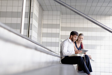 Mature man and woman sitting on steps, looking at digital tablet - ISF07513