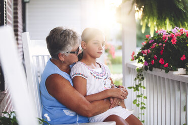 Girl sitting on grandmother's lap in porch at sunset - ISF07516