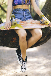 Woman with skateboard sitting on tree - ISF07521