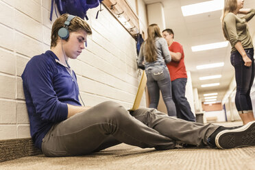 Teenager sitzt allein in der Umkleidekabine einer High School und hört Kopfhörer - ISF07557