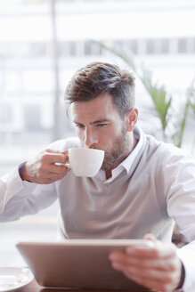 Mature man sitting in cafe, drinking coffee, using digital tablet - ISF07657