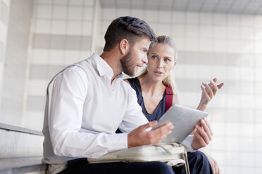 Mature man and woman sitting on steps, looking at digital tablet - ISF07681