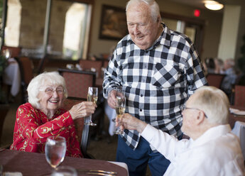 Drei ältere Erwachsene im Restaurant, die Sektgläser halten und einen Toast ausbringen - ISF07689