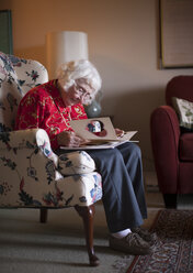 Ältere Frau sitzt auf einem Stuhl und betrachtet eine Grußkarte - ISF07699