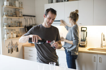 Mid adult couple pouring red wine in kitchen - ISF07758