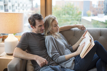 Mittleres erwachsenes Paar, das auf dem Sofa liegt und ein Buch liest - ISF07760