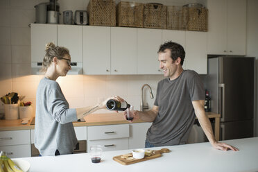 Mid adult couple pouring red wine in kitchen - ISF07764