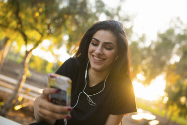 Young woman, outdoors, wearing earphones, holding smartphone - ISF07790