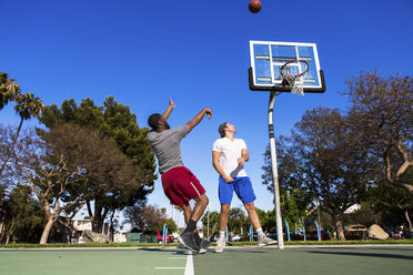 Junger Mann wirft Basketball gegen ein Basketballnetz auf einem Platz im Freien - ISF07792