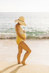 Pregnant mid adult woman wearing swimming costume holding stomach Makua beach, Hawaii, USA - ISF07807