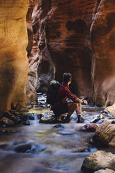 Männlicher Wanderer sitzt in einer Höhle auf einem Flussfelsen, Zion National Park, Utah, USA - ISF07810