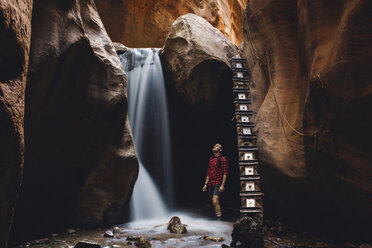 Männlicher Wanderer mit Blick auf einen Wasserfall in einer Höhle, Zion National Park, Utah, USA - ISF07812