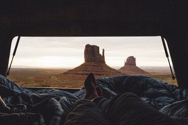 Männliche Beine und Füße, die sich in einem Geländewagen entspannen, mit Blick auf Sandsteinfelsen vom Kofferraum aus, Monument Valley, Arizona, USA - ISF07818