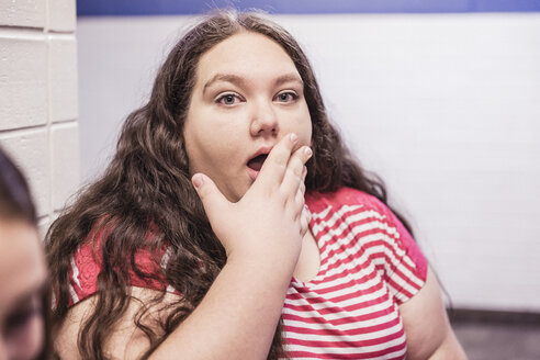 Überraschtes jugendliches High-School-Mädchen mit Hand auf dem Mund im Korridor - ISF07824