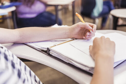 Abgeschnittene Nahaufnahme eines Teenagers, der sich am Schreibtisch in einer Highschool-Klasse Notizen macht - ISF07827