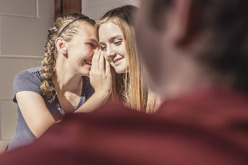 Blick über die Schulter auf zwei flüsternde Teenager-Mädchen in der High School - ISF07838