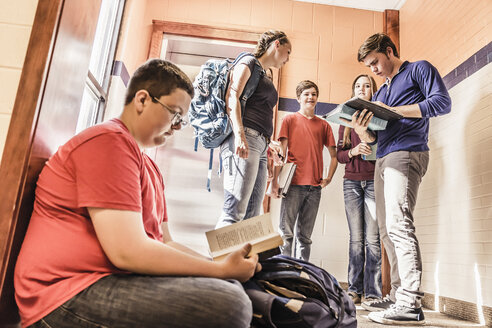 Schuljunge sitzt allein auf dem Boden und liest ein Lehrbuch im Schulkorridor - ISF07845