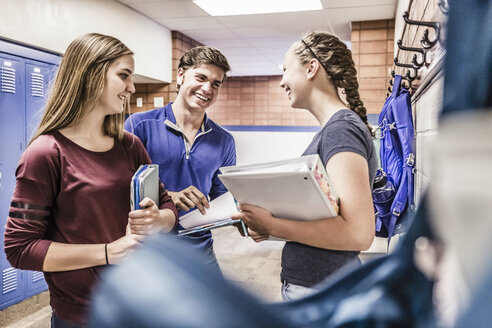 Teenager-Mädchen und Junge halten Notebooks und plaudern im Umkleideraum der High School - ISF07854