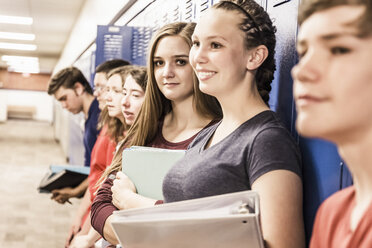 Row of teenage girls and boys holding notebooks and waiting in locker room - ISF07855