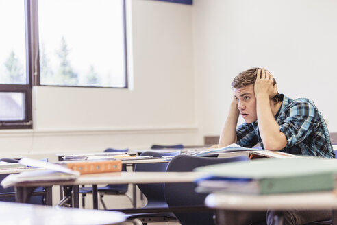 Verstörter Teenager mit dem Kopf in den Händen im Klassenzimmer einer High School - ISF07871