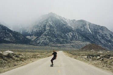 Man skateboarding on road by mountains, Lone Pine, California, USA - ISF07886