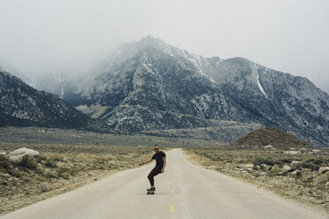 Mann fährt Skateboard auf der Straße bei den Bergen, Lone Pine, Kalifornien, USA - ISF07886