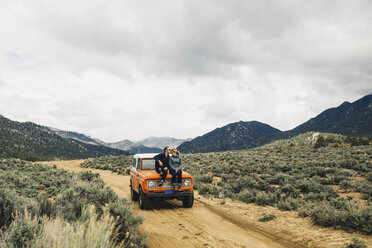 Couple sitting on vehicle in scrubland by mountains, Kennedy Meadows, California, USA - ISF07888