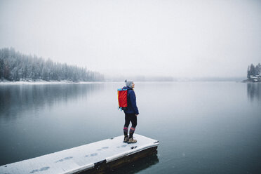 Hiker on snow covered pier looking at view of lake, Bass Lake, California, USA - ISF07895