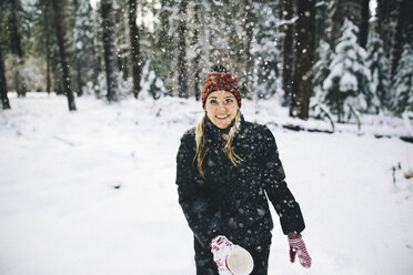 Frau in verschneitem Wald, die Schnee aus einer Tasse wirft - ISF07898