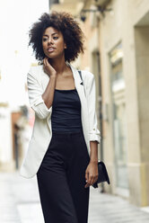 Portrait of fashionable young woman with curly hair walking in the city - JSMF00223