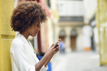 Junge Frau mit lockigem braunem Haar schaut auf ihr Handy - JSMF00228