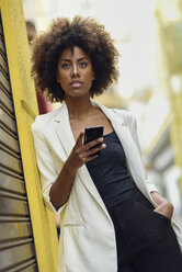 Portrait of fashionable young woman with curly brown hair and cell phone - JSMF00231