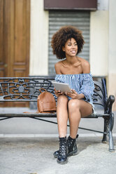 Young woman sitting on bench in the city using tablet - JSMF00259