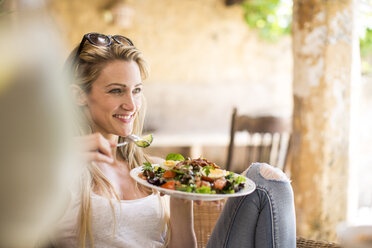 Junge Frau entspannt sich auf einer Gartenterrasse und isst Salat - CUF21350