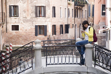 Junge Frau sitzt auf einer Kanalbrücke und betrachtet eine Digitalkamera, Venedig, Italien - CUF21482