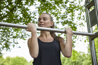 Young woman training in park, doing chin ups on exercise bars - CUF21483