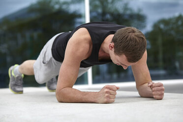 Young man training in city, doing elbow push ups - CUF21503