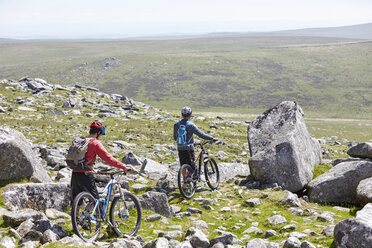 Rear view of cyclists walking bicycles down rocky hillside - CUF21584