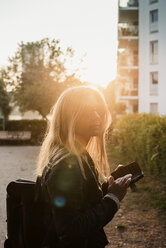 Junge Frau im Freien, bei Sonnenuntergang, mit Smartphone - CUF21608