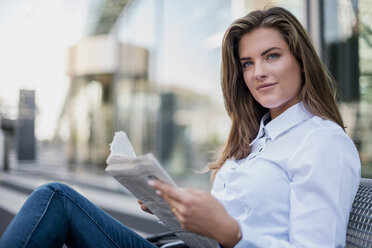 Porträt einer lächelnden jungen Geschäftsfrau, die mit einer Zeitung auf einer Bank sitzt - DIGF04568