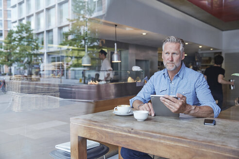 Älterer Mann, der in einem Café sitzt und ein digitales Tablet benutzt - CUF21663