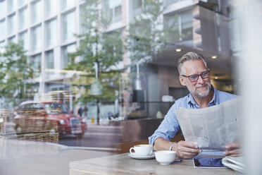 Mature man sitting in cafe, reading newspaper, street reflected in window - CUF21664