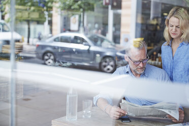 Mature man and woman in cafe, reading newspaper, street reflected in window - CUF21665