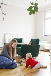Mittlere erwachsene Frau und kleine Tochter spielen mit Bauklötzen auf dem Wohnzimmerboden - CUF21707